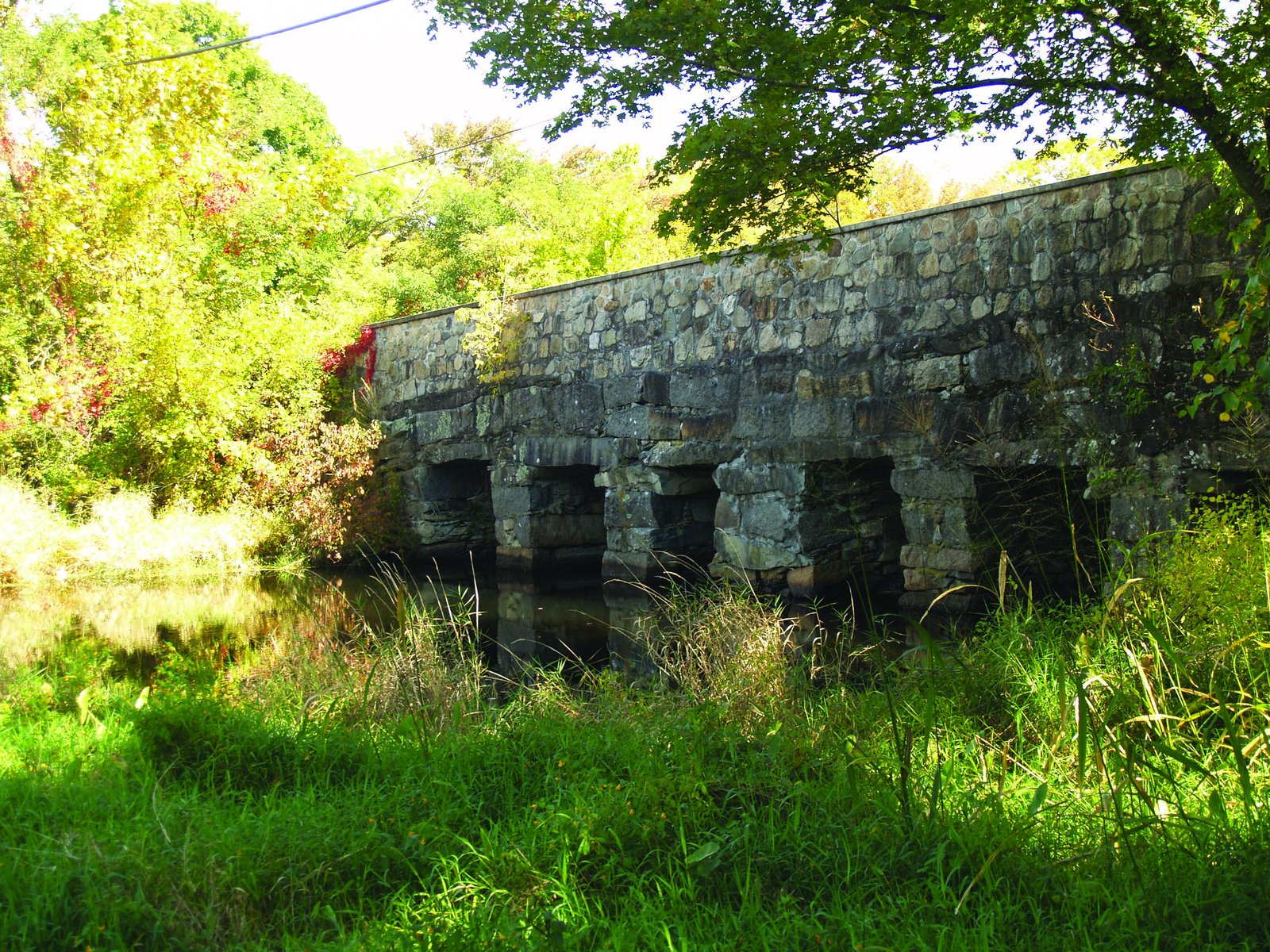 Historic stone bridge with arched openings over a stream, surrounded by trees